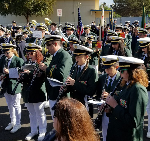 Many uniformed musicians of different ages in alignment and playing music together